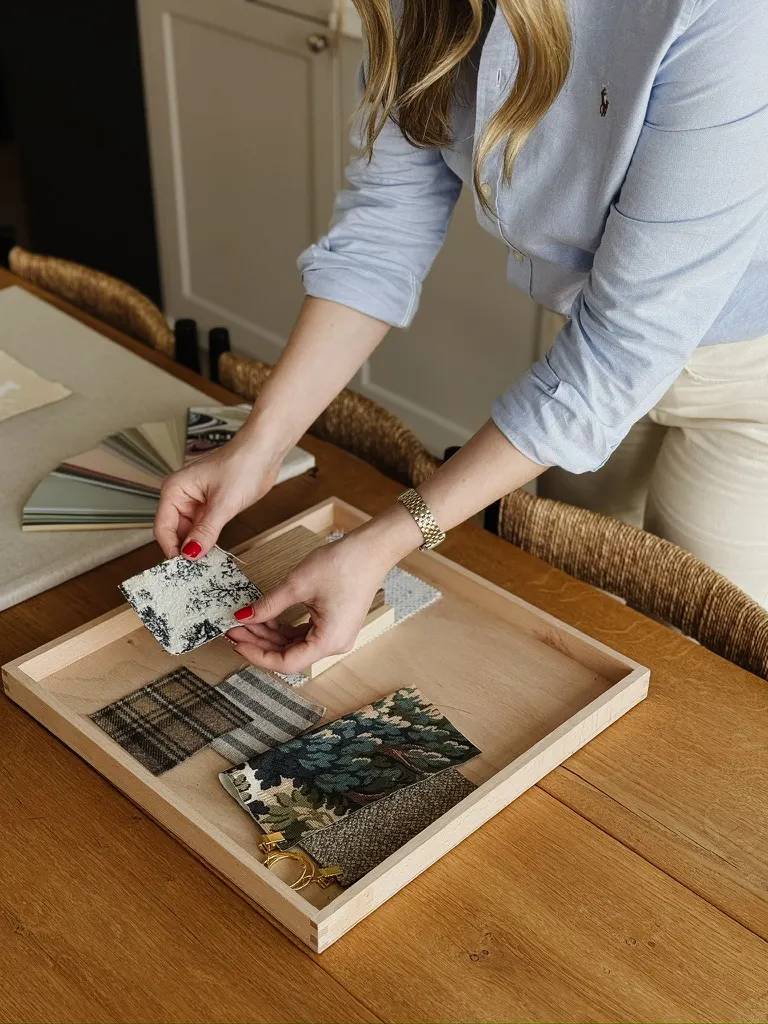 Nora-Aileen Koch legt Stoff- und Materialmuster auf ein Holztablett – Materialauswahl im Studio Olivia Interior